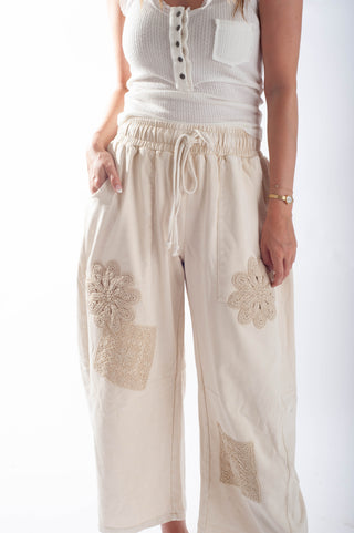 Beige pants with lace patches worn by a person on a white background