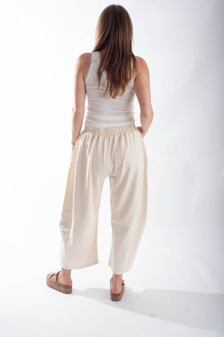 Woman wearing a white sleeveless top and beige wide-leg pants on a white background