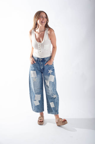 Woman wearing a white tank top and blue jeans with star patterns on a white background