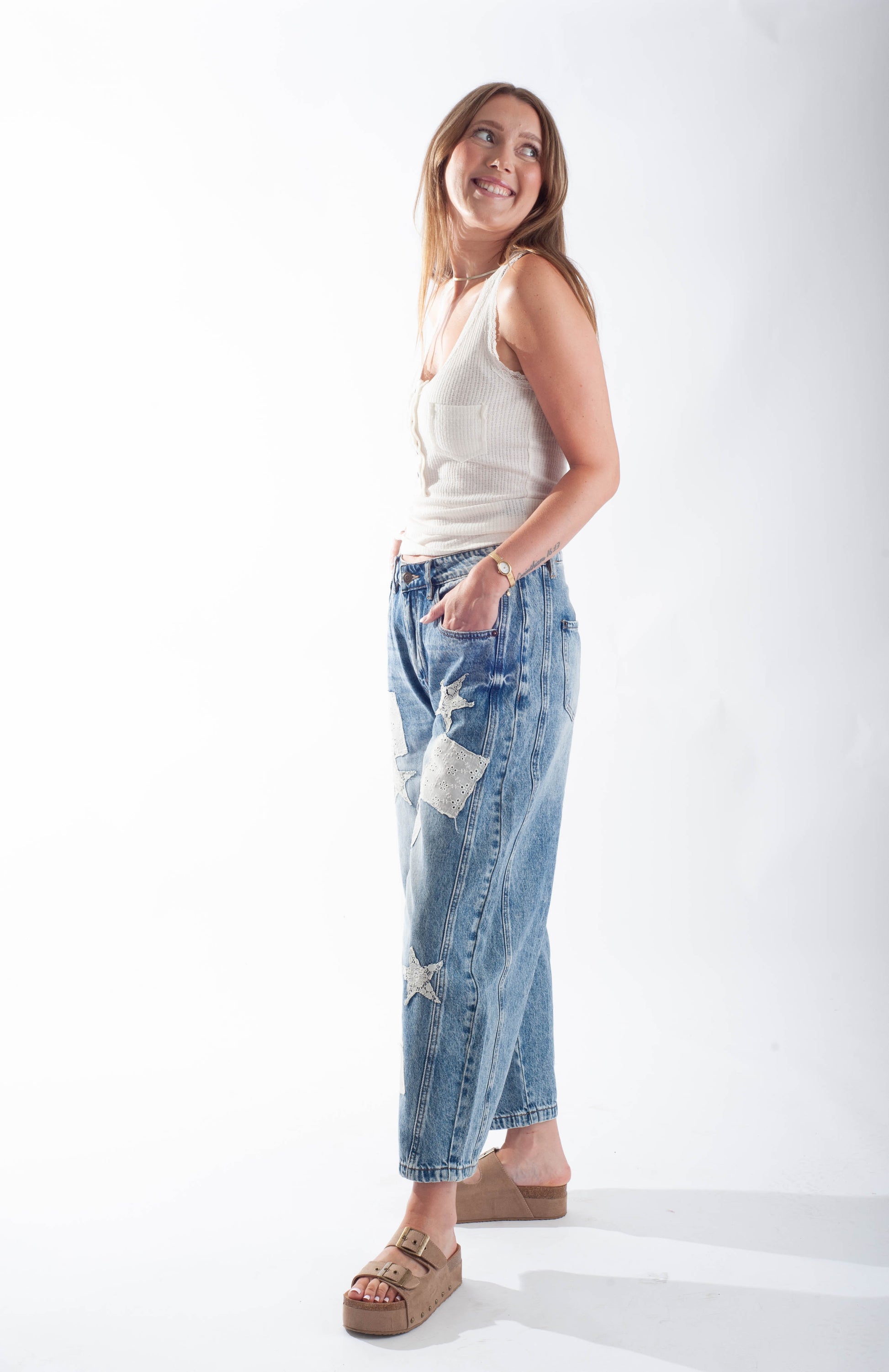 Woman wearing a white sleeveless top and blue patchwork jeans on a white background