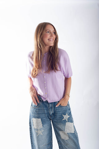 Woman wearing a light purple shirt and blue jeans with star patches on a white background