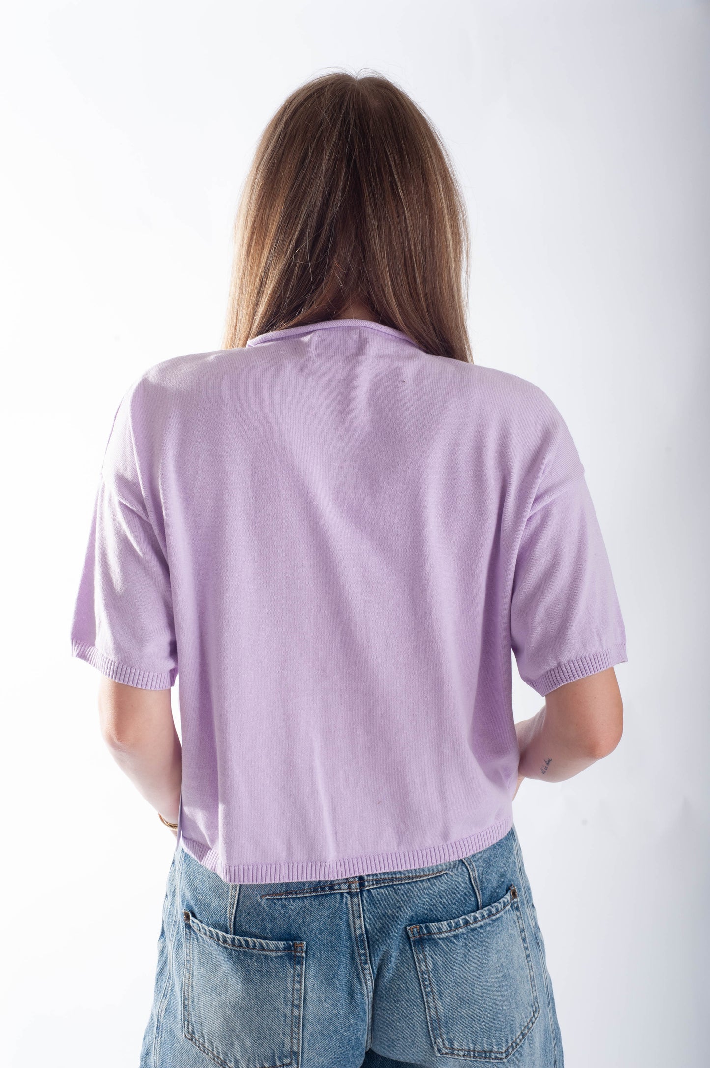 Person wearing a light purple sweater and blue jeans against a white background