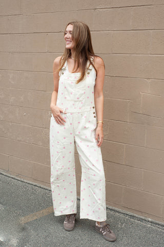 Woman wearing a white floral jumpsuit standing against a beige wall.