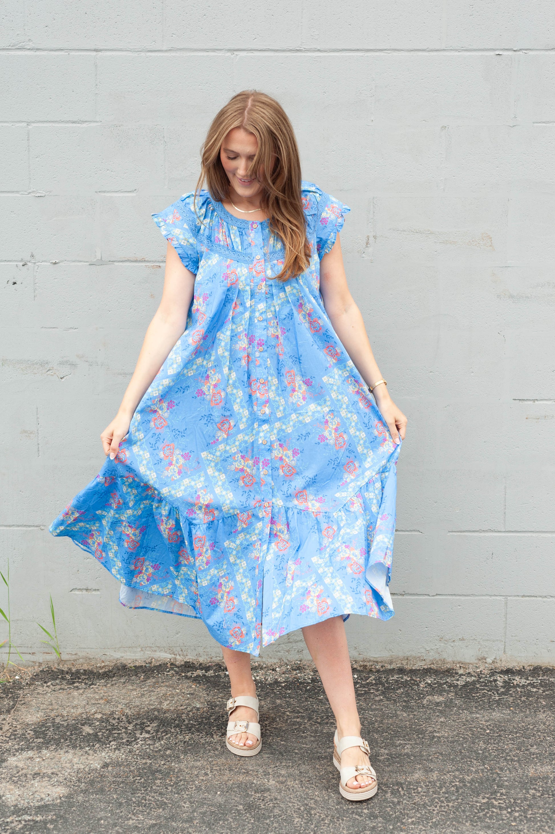 Woman wearing a blue floral dress against a gray wall.