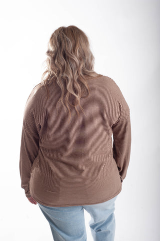 A woman viewed from behind wearing a brown and beige horizontally striped long-sleeve top and light blue jeans, set against a plain white studio background.