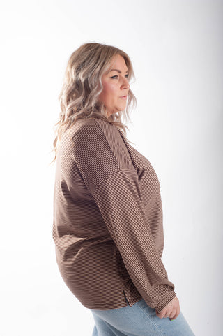 A woman wearing a brown and beige horizontally striped long-sleeve top, shown from a side profile against a plain white studio background.
