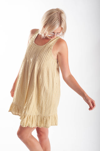 A woman wearing a sleeveless, pleated mini dress in a light cream or pale yellow color, photographed against a plain white studio background.