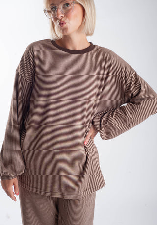 A woman wearing a brown and beige horizontally striped long-sleeve top and matching pants against a plain light gray background.