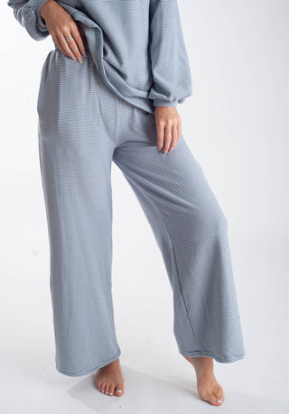A person wearing a light blue and white striped pajama set with a long-sleeve top and wide-leg pants, shown from the chest down against a plain white studio background.