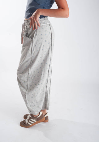 A person wearing light gray wide-leg jogger pants with a small blue floral print, paired with brown sneakers, shown from the waist down against a plain white studio background.