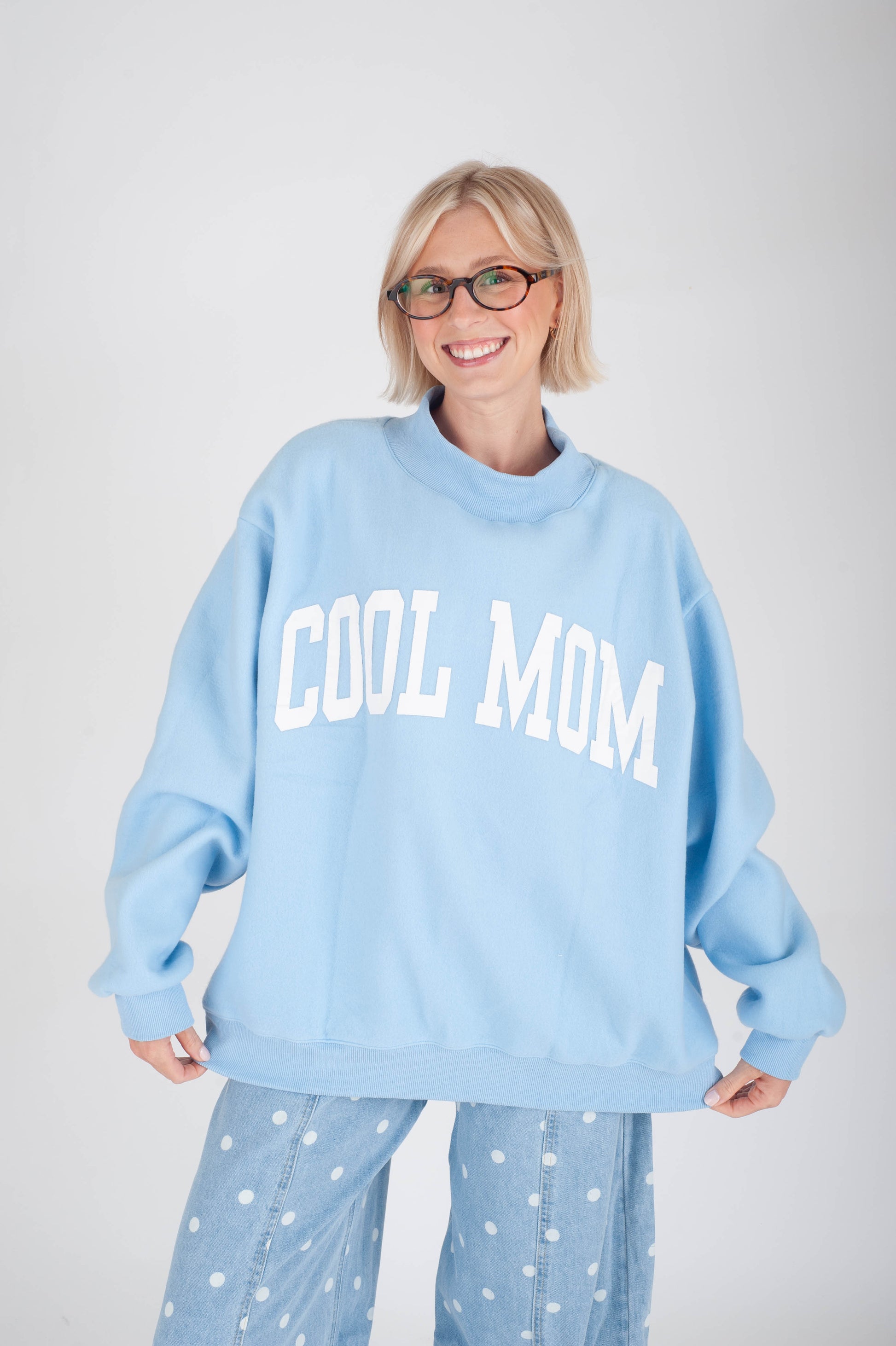 Woman wearing a light blue 'COOL MOM' sweatshirt against a white background
