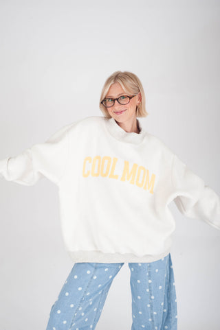 Person wearing a white sweatshirt with 'COOL MOM' text and light blue polka dot pants on a white background