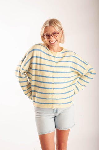 Women wearing a striped button up cardigan and denim shorts in front a neutral background.