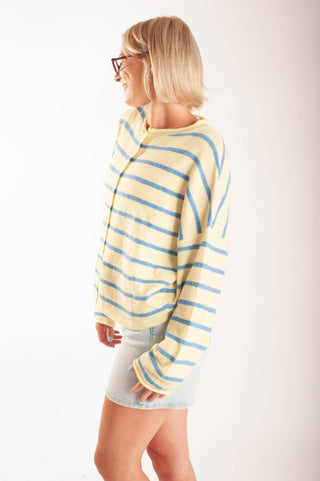 Women wearing a striped button up cardigan and denim shorts in front a neutral background.