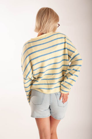 Women wearing a striped button up cardigan and denim shorts in front a neutral background.
