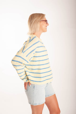 Women wearing a striped button up cardigan and denim shorts in front a neutral background.