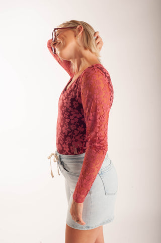 Women wearing a sheer floral lace top against a neutral background.