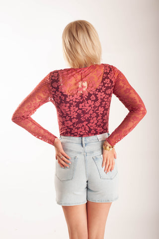 Women wearing a sheer floral lace top against a neutral background.