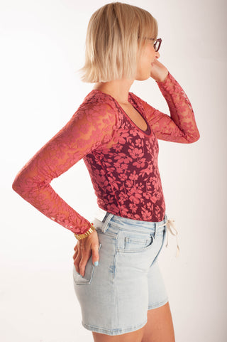 Women wearing a sheer floral lace top against a neutral background.