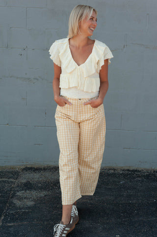 Women wearing a white top and yellow checker printed pants against a grey brick wall. 