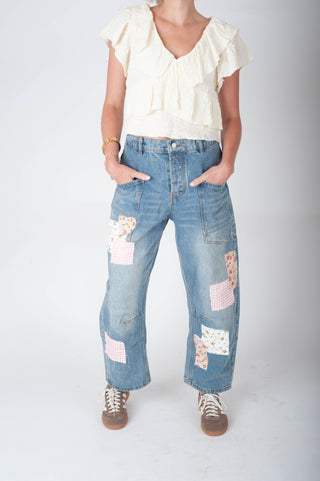 Person wearing a white blouse and blue patchwork jeans on a plain background