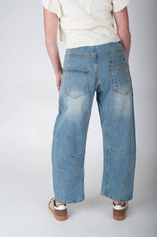 Person wearing blue wide-leg jeans and a white top on a plain background