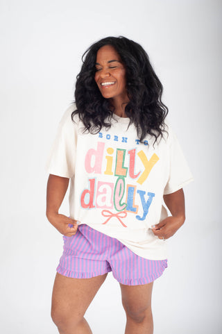 Woman wearing a colorful 'Born to Dilly Dally' t-shirt and purple shorts on a white background