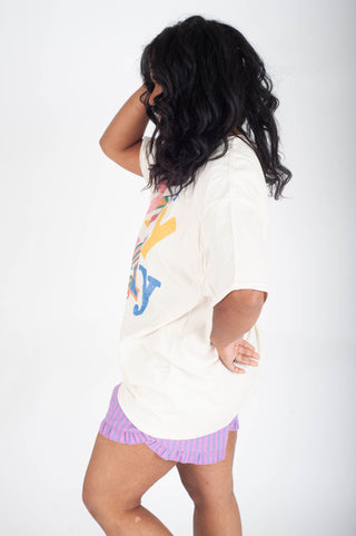 Person wearing a white oversized shirt with colorful graphics and pink shorts on a white background