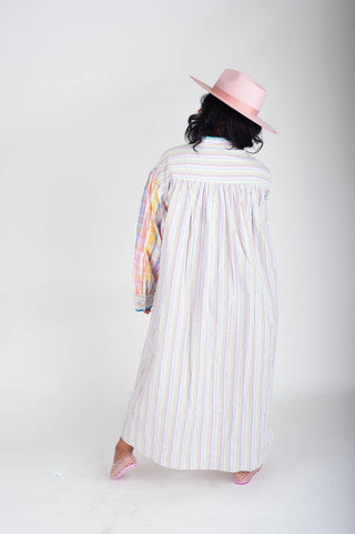Person wearing a long, light-colored dress with vertical stripes and a pink hat on a white background