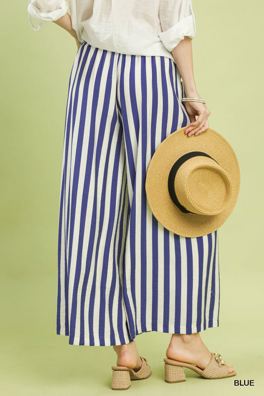 Person wearing blue and white striped pants holding a straw hat on a green background