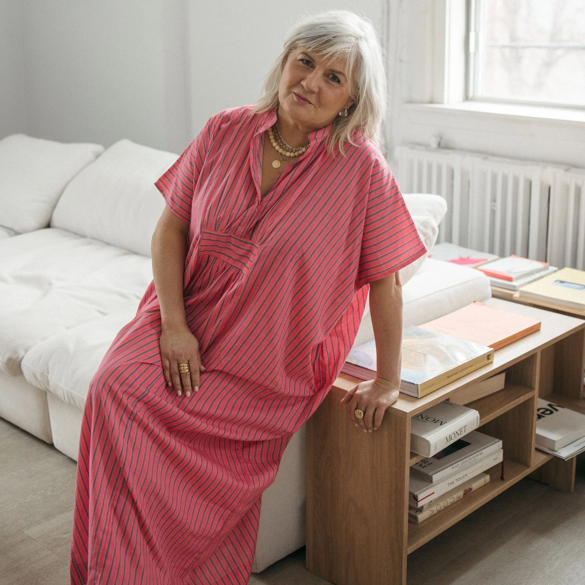 Woman in a pink dress sitting on a couch in a living room.