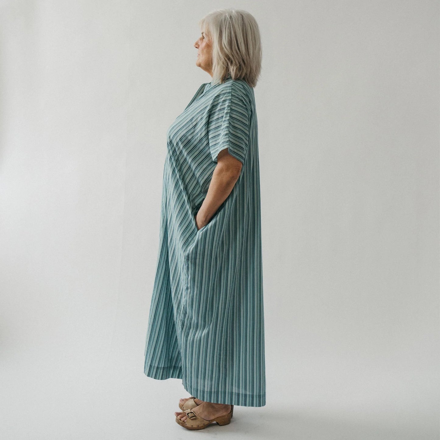 Woman wearing a long, light blue striped dress against a plain background