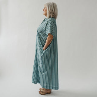 Woman wearing a long, light blue striped dress against a plain background