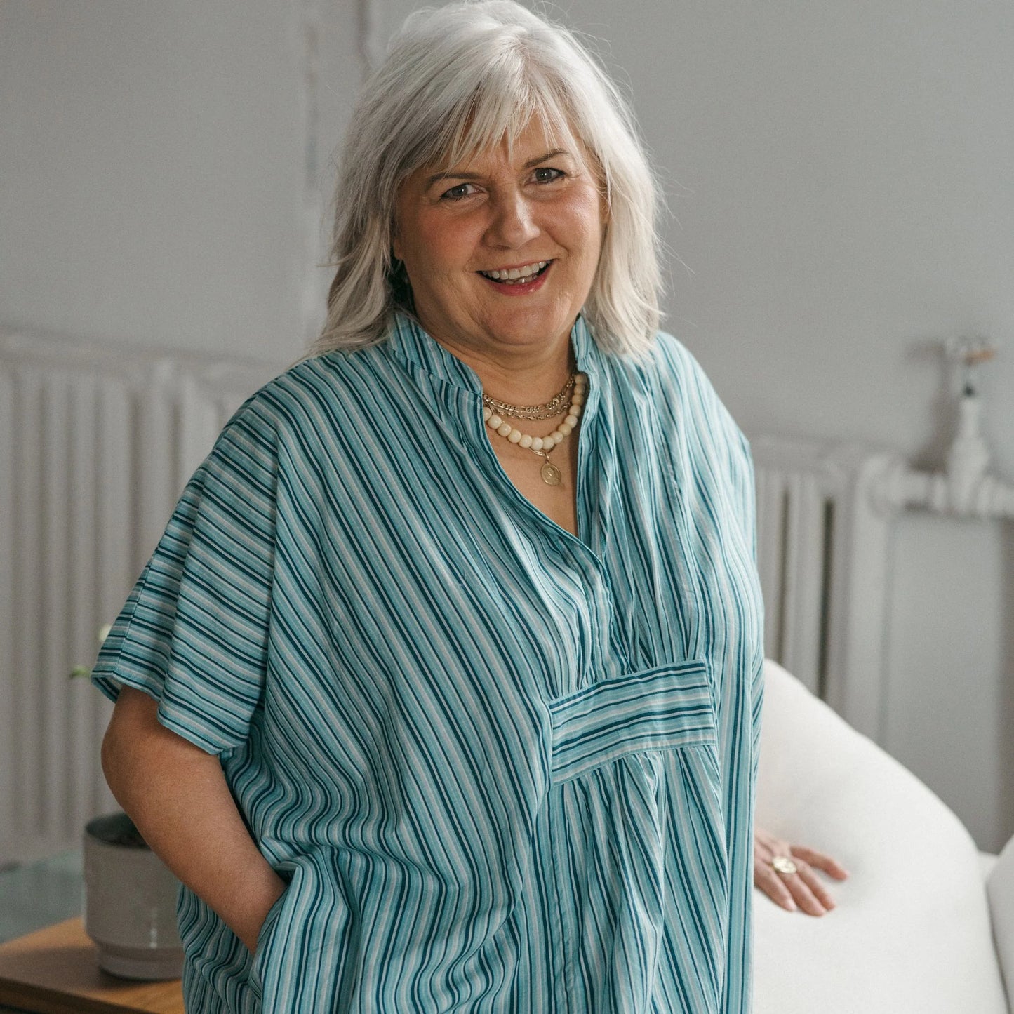 Woman wearing a blue striped shirt in a room with a white wall and radiator.