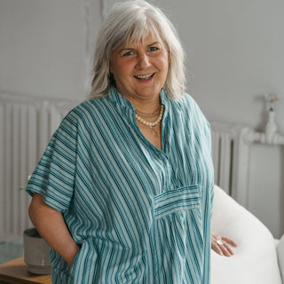 Woman wearing a blue striped shirt in a room with a white wall and radiator.
