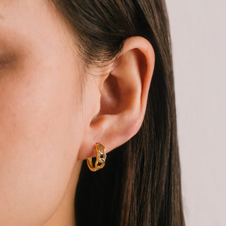 Gold hoop earring worn by a person with a neutral background.