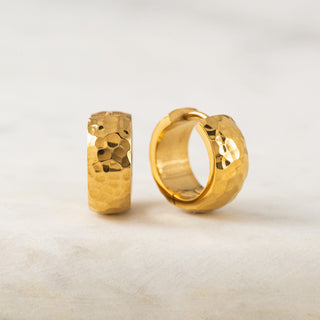 A pair of gold-colored hoop earrings with a textured surface, displayed against a neutral background.