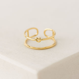 Gold ring with a knot design on a light beige background