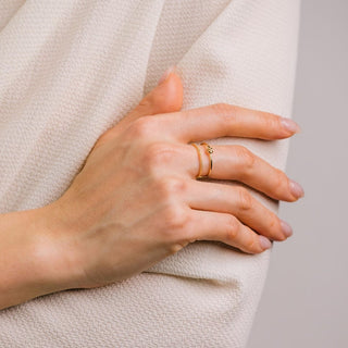 Close-up of a hand wearing a gold ring on a neutral background