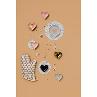 Heart-shaped ceramic items including plates, a heart-shaped bowl, and an oven mitt on a beige background.