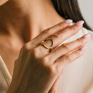 Close-up of a hand wearing a gold ring with a neutral background