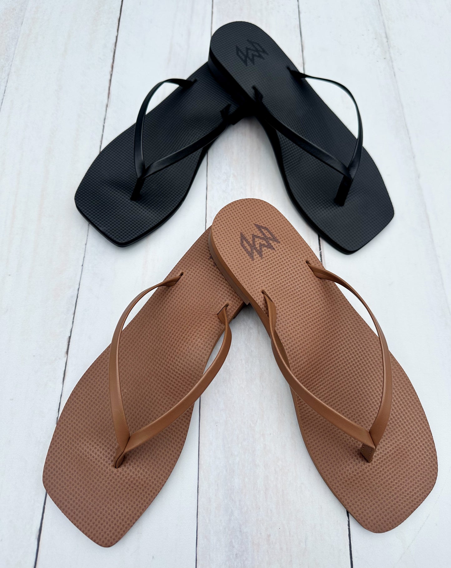 Black and brown flip-flops on a white wooden surface