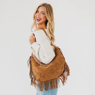 Women carrying a brown fringe shoulder bag against neutral photobackground