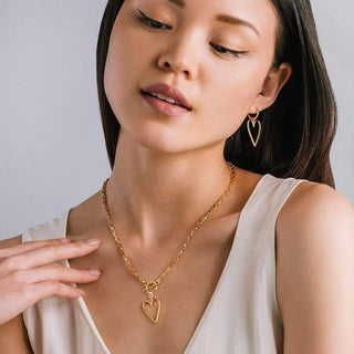 Woman wearing a gold necklace and heart-shaped earrings against a plain background