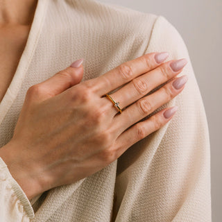 Hand wearing a gold ring with a diamond on beige fabric