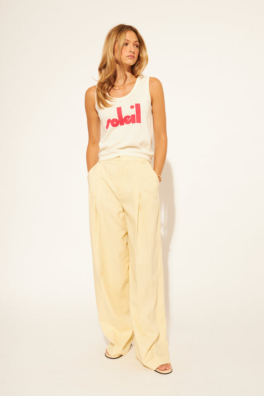 Woman wearing a white tank top with red text and light yellow pants on a white background