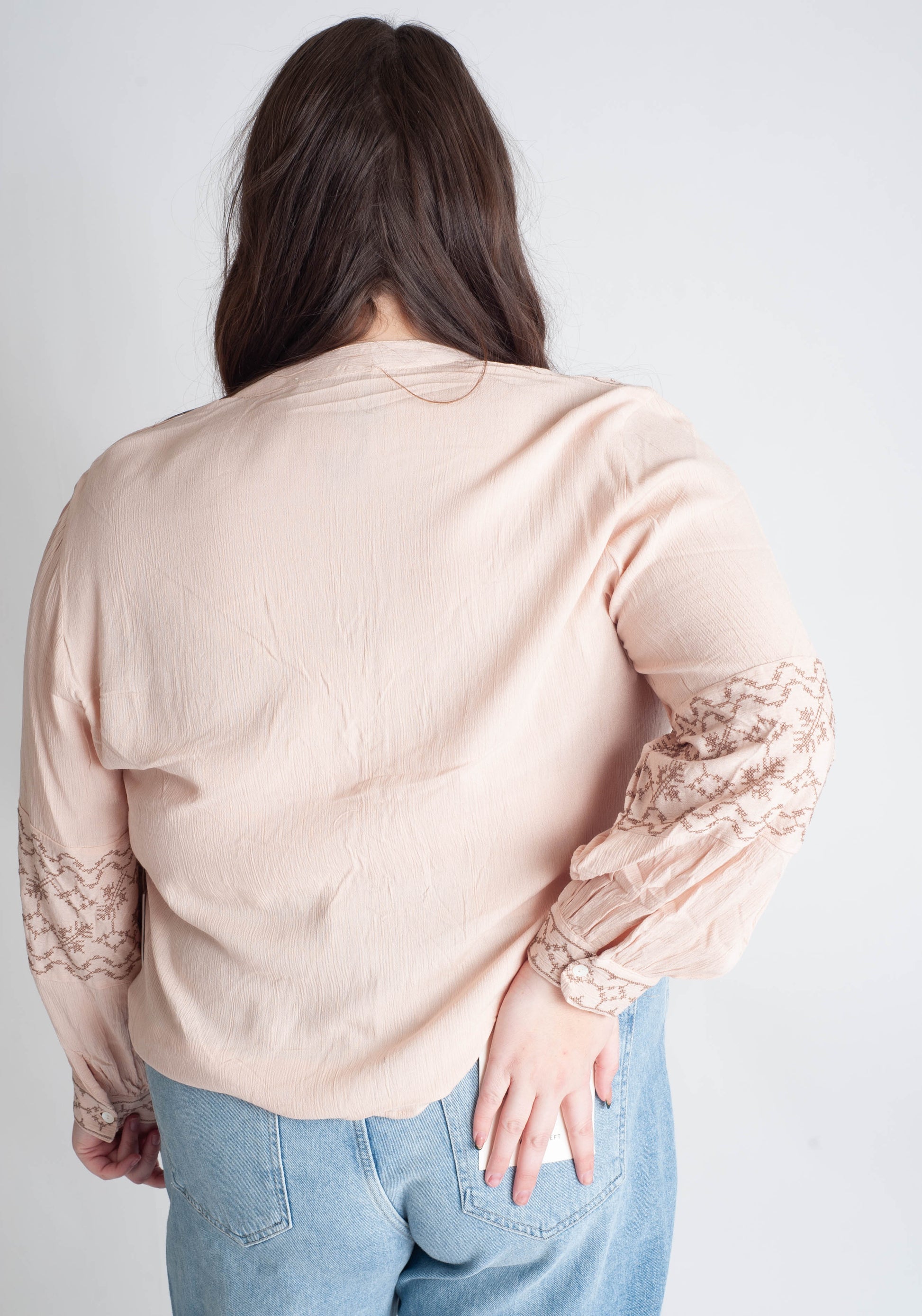 Person wearing a beige blouse with lace sleeves against a plain background
