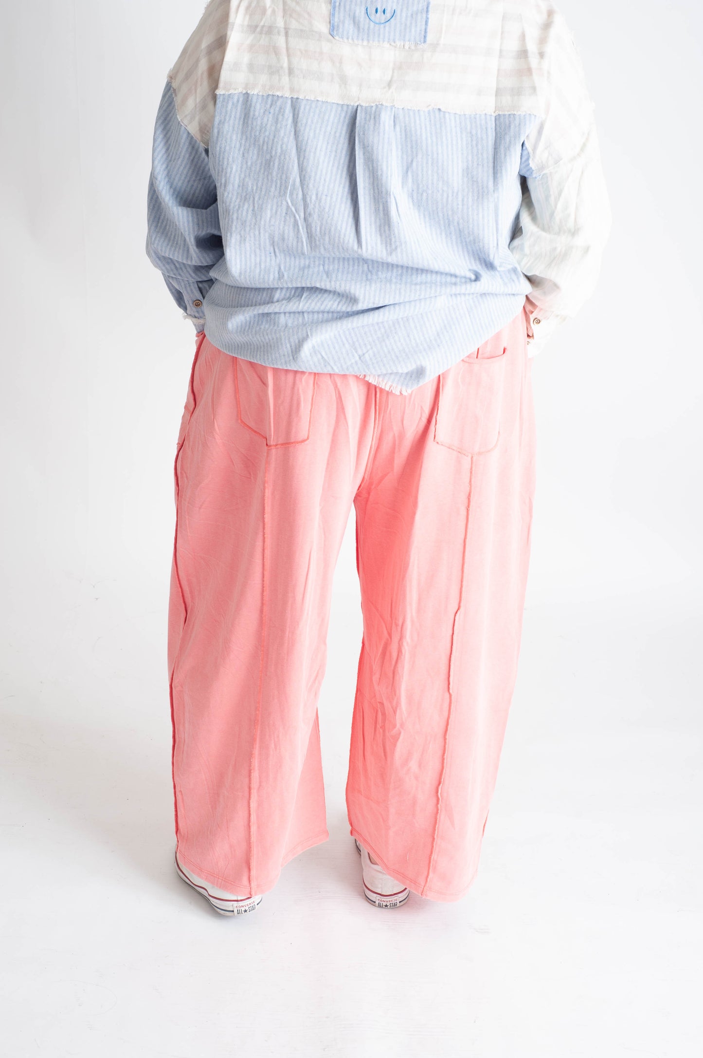 Person wearing a checkered shirt and pink pants on a white background