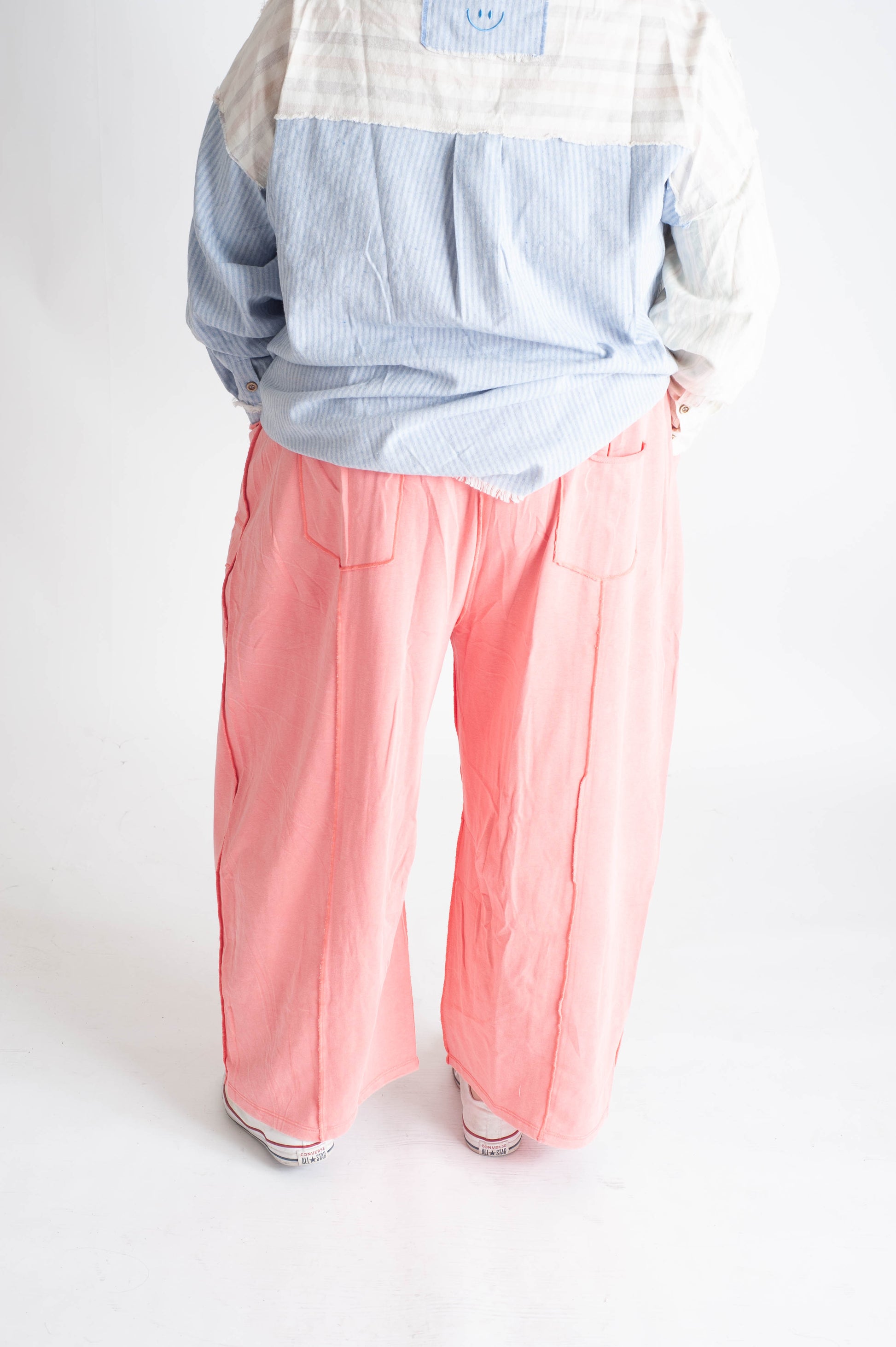 Person wearing a checkered shirt and pink pants on a white background