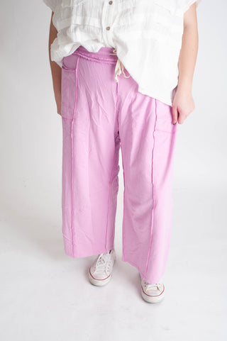 Person wearing light pink wide-leg pants and a white shirt on a white background